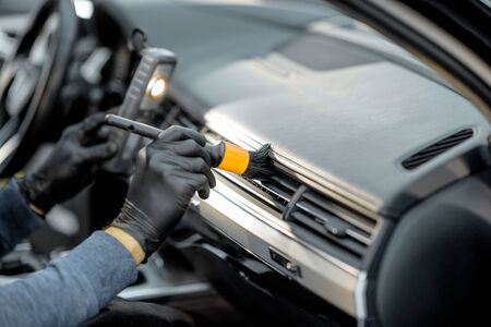 Worker provides a professional vehicle interior cleaning, wiping indoor front panel with a brush at the car service station, close-upの写真素材
