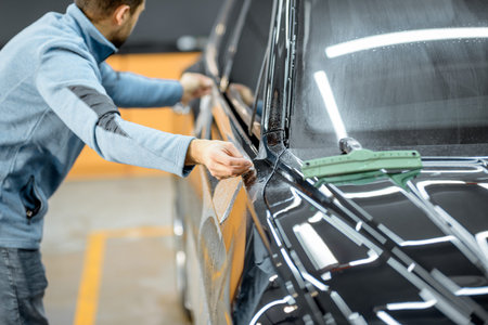 Car service worker sticking anti-gravel film on a car body for protection at the detailing vehicle workshop. Concept of car body protection with special filmsの写真素材