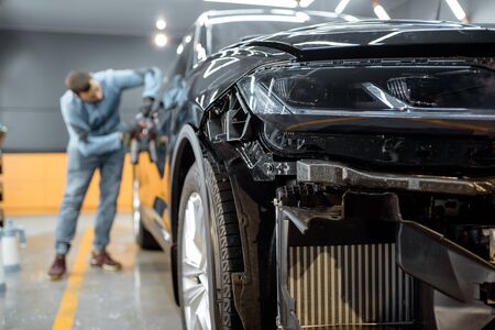 Man sticking protective film on a car body at the vehicle service station, focused on the car front. Concept of car body protection with special filmsの写真素材