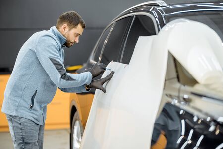 Man preparing protective film for sticking on a car body, marking it to with a pen at the vehicle service station. Concept of car body protection with special filmsの写真素材