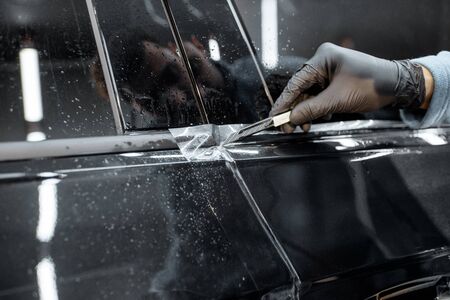 Worker trimming with cutter remains of a protective film, sticking it on a car body at the vehicle serviceの写真素材