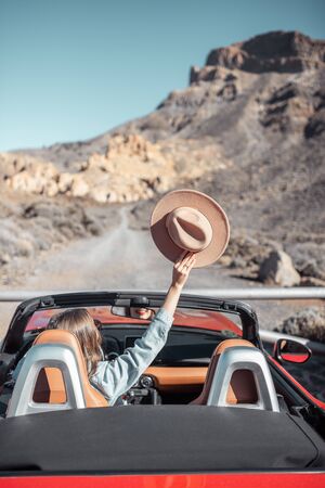 Young woman traveling by convertible car on the picturesquare road on the desert valley, rear view. Carefree lifestyle and travel conceptの写真素材