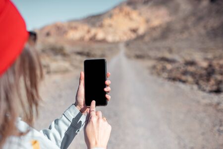 Mockup image of the smartphone with desert road on the background. Woman traveling with phoneの写真素材