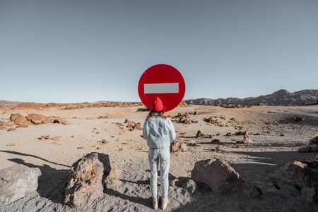 Lifestyle portrait of a woman dressed in jeans and red hat traveling on the dessert valley. standing near the traffic sign on the roadsideの写真素材