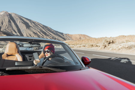 Young woman traveling by convertible car on the picturesquare desert valley, sitting at the driver...