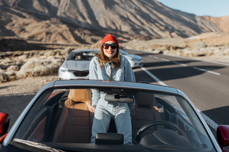 Lifestyle portrait of a young woman enjoying road trip on the desert valley, getting out the...