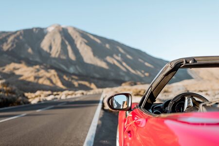 Convertible car on the roadside of the desert valley with volcano on the background, traveling by car conceptの写真素材