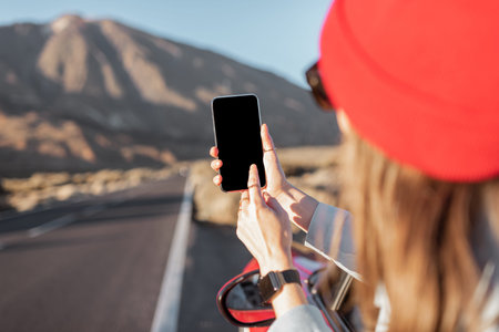 Woman traveling by car on the volcanic valley, leaning out of the car window, photographing with a...