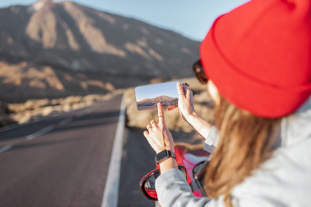 Woman traveling by car on the volcanic valley, leaning out of the car window, photographing with a...