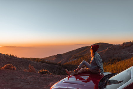 Landscape view on the roadside above the clouds with woman enjoying beautiful sunset, sitting on the...