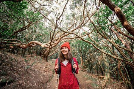 Portrait of a happy woman dressed casually in red shirt and hat hiking in the beautiful rainforest while traveling on Tenerife island, Spainの写真素材