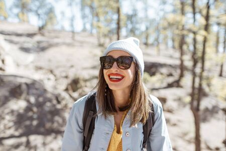 Lifestyle portrait of a happy sylish woman in hat and sunglasses hiking with backpack in the forest on a sunny dayの写真素材