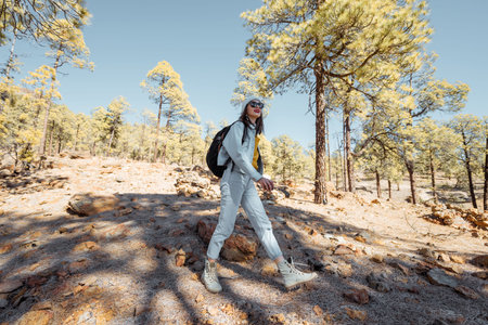 Young woman dressed casually walking with backpack in the forest highly in the mountains on the...