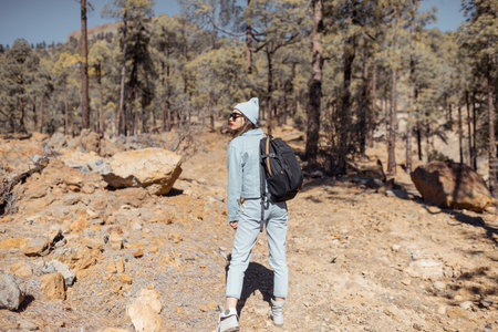 Young woman dressed casually walking with backpack in the forest highly in the mountains on the...