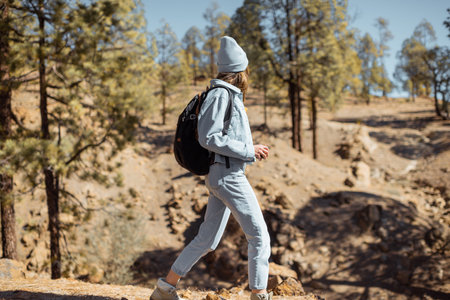 Young woman dressed casually walking with backpack in the forest highly in the mountains on the...