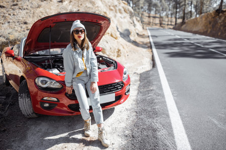 Frustrated woman standing on the roadside, having some problems with a car while traveling alone at...