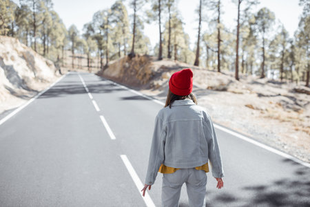 Lifestyle portrait of a stylish woman running on the beautiful mountain road, feeling happy and carefree while traveling. View from the backsideの写真素材