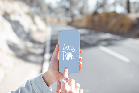 Woman holding smart phone with a text about traveling on the mountain road background, Close-up view