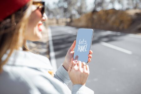 Happy woman holding smart phone with a text about traveling on the mountain road backgroundの写真素材