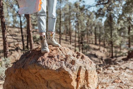 Woman standing on the stones with map, hiking on a rocky land, close-up on legs in trekking shoes