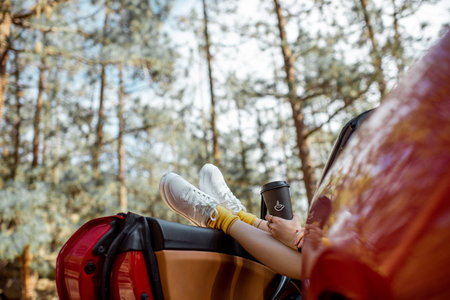 Woman traveling by convertible car on nature, pulling her legs out the car window on the roadside in...