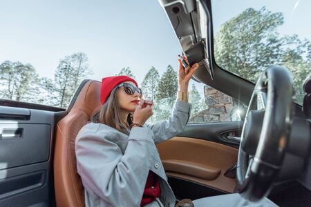 Woman applying makeup, drawing lips while sitting on the driver's seat of convertible carの写真素材