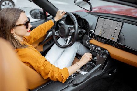 Young and cheerful woman driving sports car with a digital touchscreen with launched controlling...