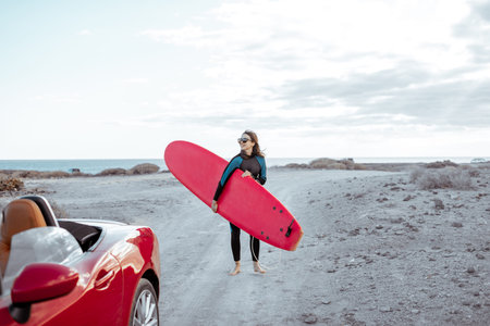 Portrait of a young woman surfer in swimsuit walking with surfboard on the dirt road near the ocean....