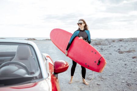 Portrait of a young woman surfer in swimsuit walking with surfboard on the dirt road near the ocean. Active lifestyle and surfing conceptの写真素材