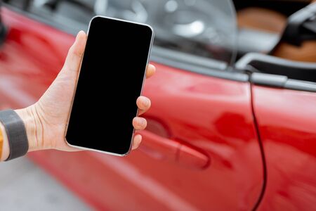 Woman holding smartphone near the car door, close-up view on phone with black screen to copy paste. Car remote control conceptの写真素材