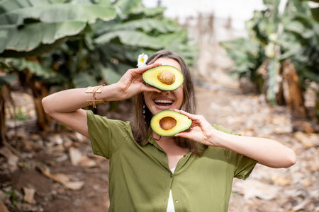 Portrait of a young smiling woman hiding her face with sliced avocado outdoors. Concept of...