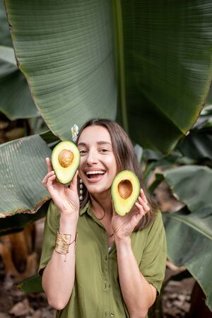 Portrait of a young and cute woman with sliced avocado berry in the banana leaves outdoors. Concept of vegetarianism, healthy eating and wellbeingの写真素材