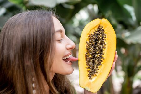 Portrait of a young woman licking papaya fruit, closeup view outdoors. Concept of vegetarianism, healthy eating or intimate healthの写真素材