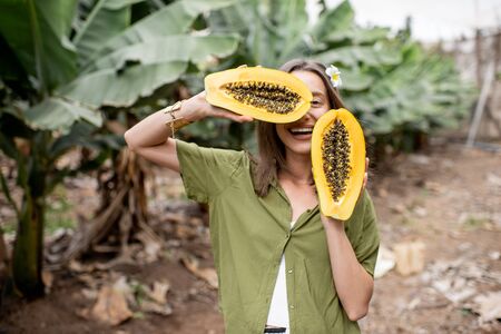 Portrait of a young woman with sliced papaya fruit on the plantation. Concept of vegetarianism, healthy eating of fresh fruits, skin care and wellbeingの写真素材