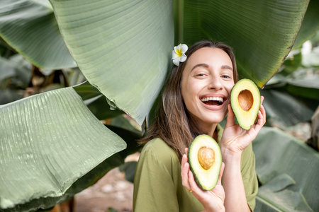 Portrait of a young and cute woman with sliced avocado berry in the banana leaves outdoors. Concept...