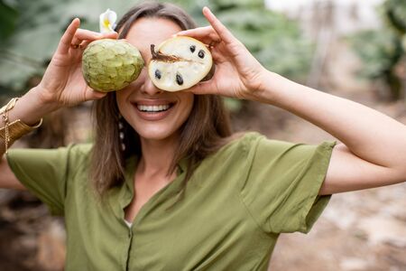 Closeup portrait of a young woman hiding her face behind Annona Cherimoya exotic fruit outdoors. Concept of vegetarianism, healthy eating fresh exotic fruits and wellbeingの写真素材