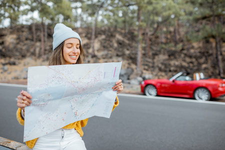 Portrait of a young stylish woman with paper map on the road side, traveling in the forest