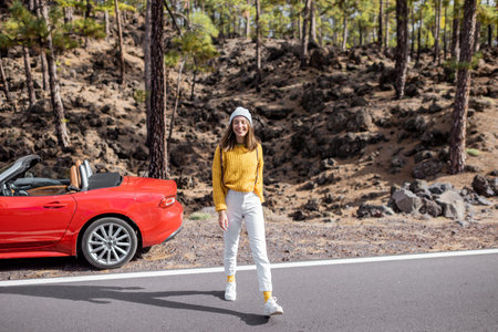 Young stylish woman walking on the mountain road, while traveling by car. Carefree lifestyle and...