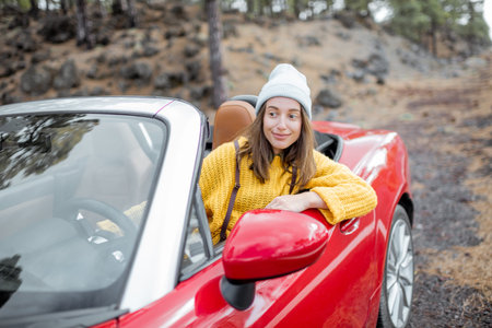 Portrait of a stylish woman in yellow sweater sitting on the drivers seat of convertible sports car on the roadside. Carefree lifestyle and traveling conceptの写真素材
