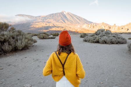 Stylish woman in bright clothes on the beautiful volcanic valley with volcano on the background during a sunset. Traveling on Tenerife island, Spainの写真素材