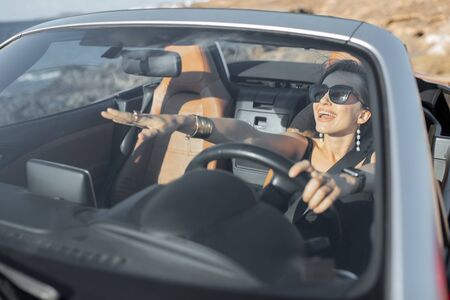 Portrait of a young woman driving a cabriolet near the ocean on a summer time. View through the windshield. Concept of a carefree travel and summer timeの写真素材