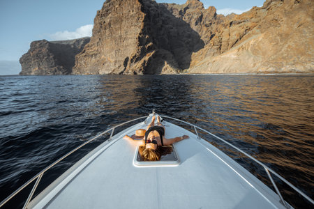 Woman enjoying ocean voyage, lying on the yacht nose while sailing near the breathtaking rocky coast...