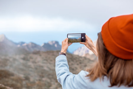 Woman photographing on phone beautiful landscapes, traveling highly in the mountains on Tenerife...