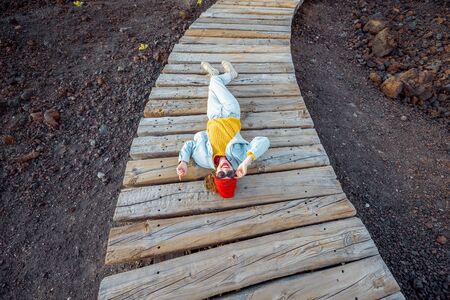 Woman dressed in bright lying on the wavy boardwalk through the rocky volcanic land, enjoying a trip on the island, view from aboveの写真素材