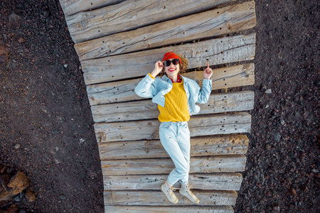 Portrait of a young stylish woman dressed in bright clothes lying on the wooden pathway outdoors