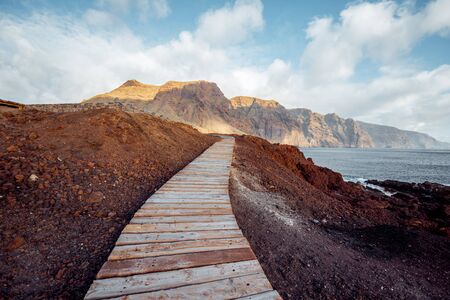 Landscape with picturesque wooden pathway through the rocky land and mountains on the background. North-west cape of Tenerife island, Spainの写真素材