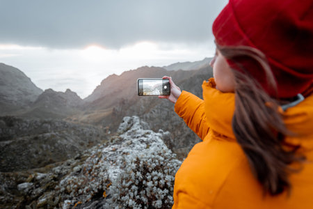 Young woman dressed in bright jacket and hat photographing on phone breathtaking views on the...