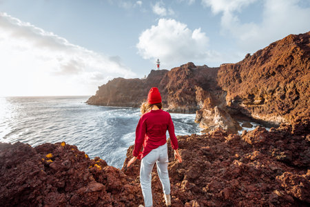 Woman enjoying great views on the rocky ocean coast and a lighthouse on the background, traveling on...