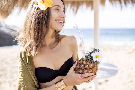 Portrait of a beautiful young woman with exotic cocktail at the beach resort on a sunny day. Concept of exotic summer vacations, beauty and wellnessの写真素材