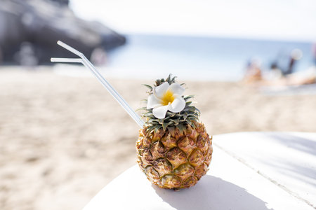 Exotic summer cocktail made in pineapple fruit decorated with flower on the beach. Concept of a...